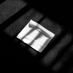 Folded white cloth on dark textured floor, sunlit shadows
