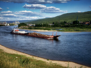 A warm summer day, a river, a self-propelled barge with various cargoes sailing along the river, cloudy sky