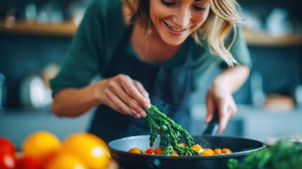 A woman is cooking in the kitchen, adding asparagus to a pan with other vegetables, smiling with joy.