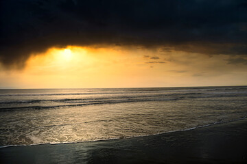 Dramatic sunset over ocean waves with dark storm clouds and golden sky
