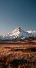 Majestic Snow Capped Mountain Peak Overlooking Golden Dry Grass Field at Sunrise.