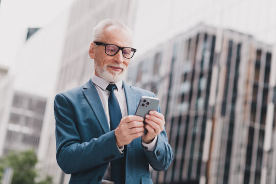 Confident senior businessman in a suit using smartphone in urban setting showcasing success and professionalism