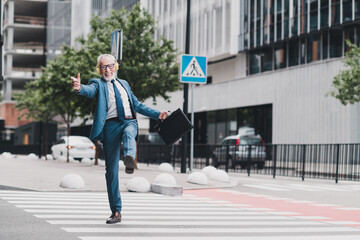 Obraz premium Energetic senior businessman walking outside wearing a suit and headphones in an urban city environment