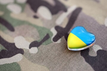 Glass heart with Ukrainian flag lies on military camouflage fabric. Concept of support Ukraine
