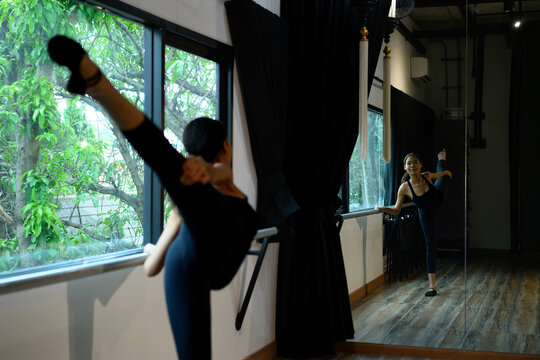 Young woman practicing ballet stretch at barre with leg raised high.