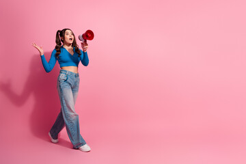 Young woman with megaphone posing against pink background, expressing excitement and confidence in stylish casual attire
