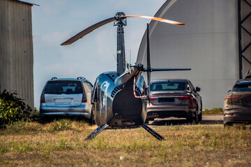 A black helicopter stands in front of two cars	
