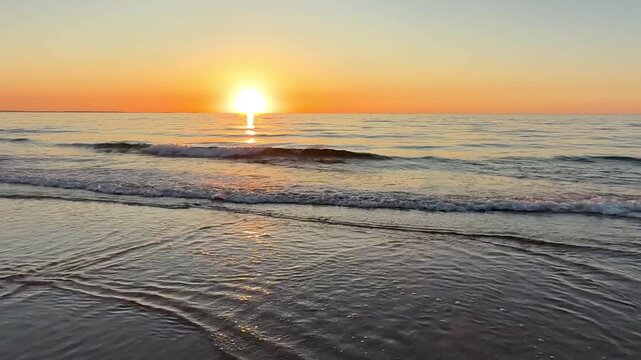 beautiful sunset over tranquil beach with gentle waves rolling onto the shore, vibrant clouds illuminated by golden light of the setting sun
