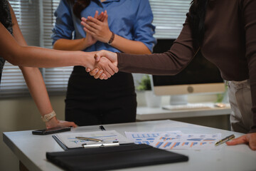 Businesswomen shaking hands in a corporate office, colleagues celebrating successful partnership deal and agreement
