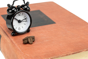 Black alarm clock and coffee beans on an old book, signifying an intense study session or working late to meet a deadline isolated on white background with clipping path.