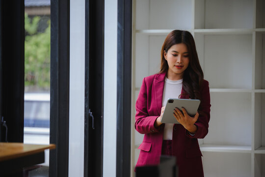 Asian businesswoman using tablet, standing in modern office, managing business data and digital tasks