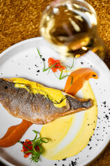 Gourmet fish fillet with crispy skin, plated with colorful sauces, fish roe, herbs, and black crumbs. Elegant fine dining presentation with white wine pairing