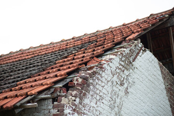 A rustic brick wall with visible damage along the roof edge and broken tiles.