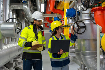 Male and female engineers inspecting HVAC chillers, pipelines, and control panels in a factory setting emphasizing safety and teamwork.