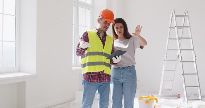 Foreman worker and female client supervises and directs worker meeting looking at project plan, holding blueprints, planning work, discussion with construction engineer in hardhat, architect talk