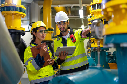 A man and woman engineer inspect a compressor and pipeline, focusing on infrastructure and production in a factory.
