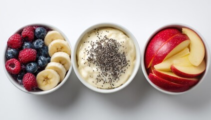 Three small white bowls, each containing a healthy breakfast.  Bowl one has berries, bowl two has yogurt and seeds, bowl three has sliced apples.  All sit on a plain white background