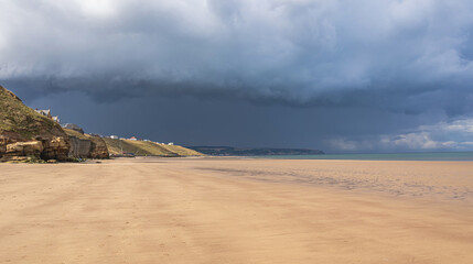 A seaside scene of a sunny beach with dark clouds forming in the distance.