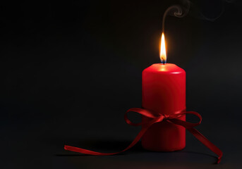 Red candle with ribbon burns brightly against dark background, creating warm and serene atmosphere. gentle smoke adds touch of elegance to scene