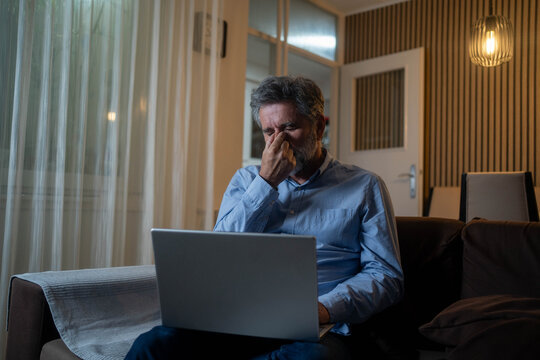Stressed mature man sitting in living room at night with laptop