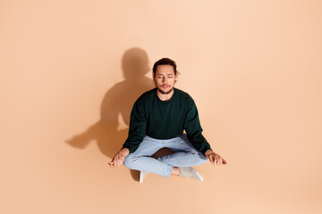 Young man seated in a meditative pose on beige background showcasing calmness and focus, ideal for mindfulness and wellness themes