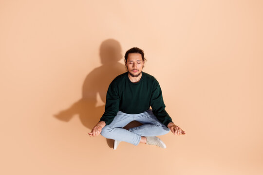 Young man seated in a meditative pose on beige background showcasing calmness and focus, ideal for mindfulness and wellness themes
