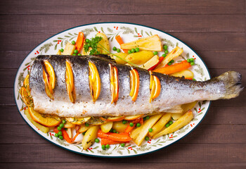 Roasted salmon with lemon, oranges and herbs served with vegetables on oval plate. View from above, top studio shot