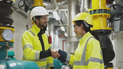 Two technicians shake hands after agreeing on a solution for a refrigeration system in a factory boiler room.
