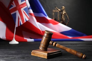 Judge's gavel, flags of United Kingdom and statue of Lady Justice on black wooden table, closeup