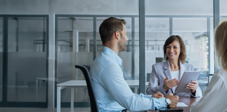 Team mature ceo businesswoman mentor discussing project with young european colleagues on tablet sitting in office. Professional business people working together using technology. Banner, copy space - Powered by Adobe