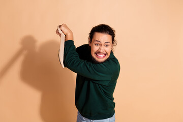 Young man in green pullover holding and smashing object with expressive look on beige background