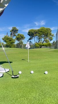 A person is playing golf and is about to hit a ball with a golf club. The scene is set on a green golf course with trees in the background
