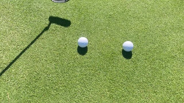 A golf course with a black and white golf club and three white golf balls. The golf balls are in a row and the club is next to them