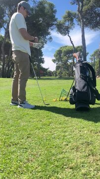 A man is standing on a golf course with his golf bag. He is looking at his phone