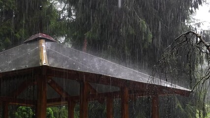Heavy rain falls on the roof of a gazebo in a garden in slow motion - Powered by Adobe