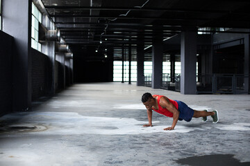 African American man performing push-up on warehouse floor by columns and tall windows, copy space
