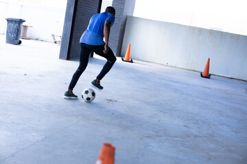 African American male athlete dribbling soccer ball past orange cones in parking garage, copy space