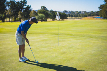 Senior golfer lining up putt on putting green with putter, golf ball near flagstick, copy space