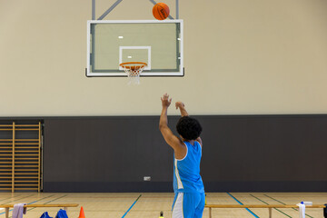African American male practicing jump shot under orange rim with basketball on court, copy space