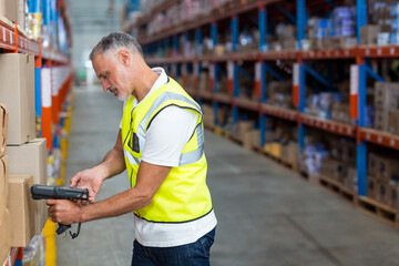Warehouse worker scanning package with barcode scanner near stacked boxes on blue racks in aisle