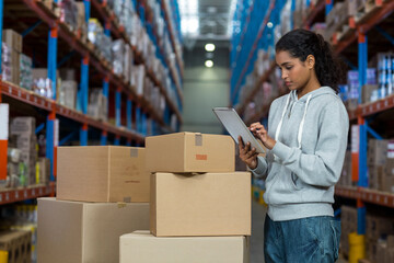 Asian worker holding tablet standing in warehouse aisle with shelves holding boxes under lights
