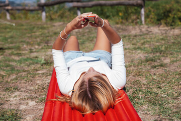 Woman lying on red camping mat checking smartphone outdoors