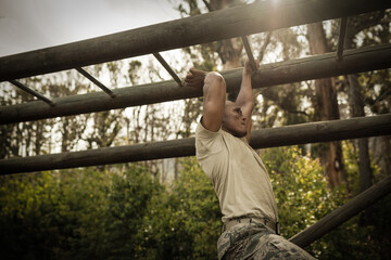 African American man crossing metal bars on forest obstacle course wearing utility belt, copy space