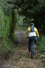 Obraz premium Mid adult man wearing bike jacket, cycling helmet riding mountain bike on forest path with backpack