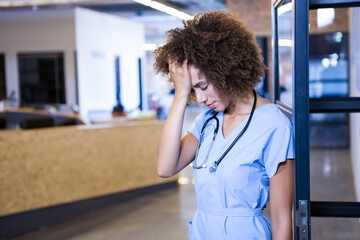 Nurse leaning on glass partition at reception desk pressing forehead with stethoscope