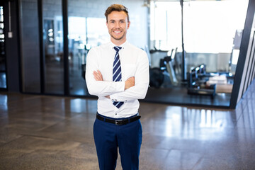 Fototapeta premium Businessman standing with crossed arms in office gym with glass partitions and exercise bikes
