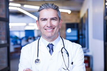 Middle-aged doctor standing in glass-walled corridor wearing lab coat and stethoscope, LED-lit