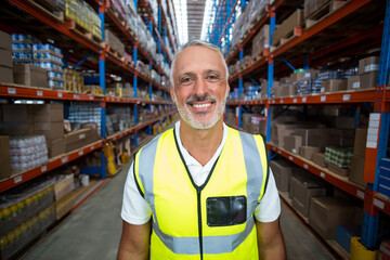 Naklejka premium Warehouse supervisor wearing neon yellow vest in aisle with metal shelves of boxes under lights