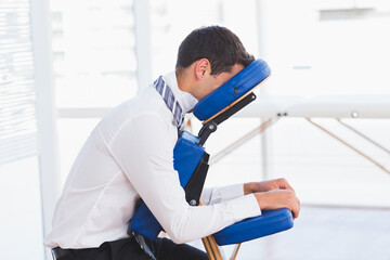 Man in business attire sitting on blue massage chair in wellness room leaning forward