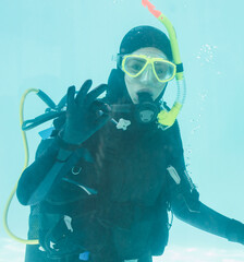 Scuba diver is signaling OK underwater with yellow diving mask and regulator in turquoise pool
